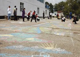 People drawing with chalk on a sidewalk outdoors.