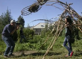 People building a large dragon made from sticks outdoors in a yard with a house and trees in the background.