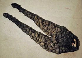 A pair of dark, elongated objects made from small, rounded stones, resembling a pair of scissors or pliers with open jaws, laid on a white surface.