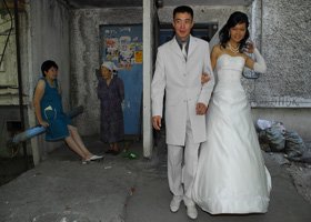 A bride and groom walking together in an outdoor setting with a woman sitting on a bench and two other women standing nearby.