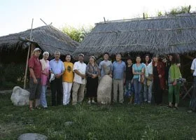 Group of people standing outdoors in front of rustic thatched-roof buildings