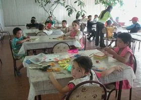 Children sitting at tables in a classroom, engaging in various activities and eating snacks.