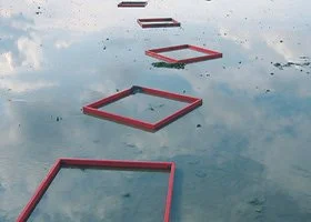 Floating red square and rectangular frames on calm water, creating a pathway leading into the distance.