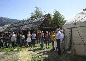 Group of people gathered outdoors near traditional huts in a rural setting.