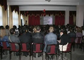 A large group of people seated in an auditorium watching a presentation on a screen.