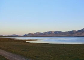 Calm lake with mountains in the distance and a clear blue sky.