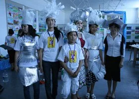 Group of young people dressed in costumes and uniforms, standing in an industrial or laboratory setting with blue lighting.