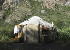 A traditional yurt set against a grassy landscape with hills in the background, outdoor laundry hanging to dry.