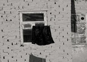 A window with a black piece of cloth hanging outside and covering part of the window, on a brick wall.