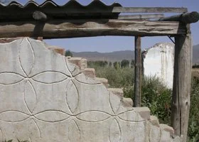 Stone wall with carved geometric patterns under a wooden structure, outdoor landscape background