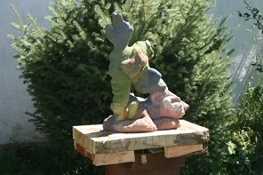 A garden sculpture of an angel with wings, standing on a base, placed on a wooden platform outdoors.