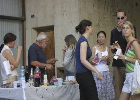 Group of people standing around a table with drinks and food in an indoor setting, engaging in conversation.