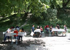 People sitting at tables outdoors under trees in a park.