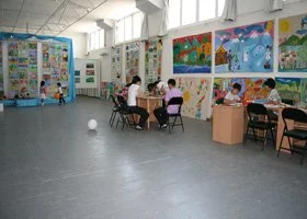 Children sitting at tables in a brightly lit art classroom with colorful artwork displayed on the walls.