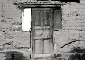 Old wooden door in a cracked brick wall with a small, rectangular opening