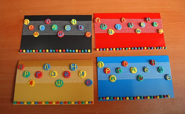 Four colorful handmade boards with lettered circular cutouts placed on a wooden surface.