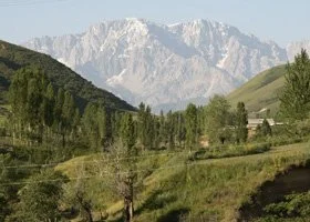 Scenic landscape of green hills, forested areas, and distant mountains under a blue sky.