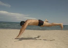 A man performing a plank exercise on the beach with the ocean in the background.