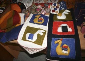 Three handmade fabric pouches with animal and letter designs, placed on a colorful table with various crafts and sewing supplies around them.
