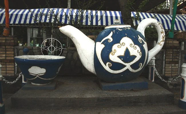 Large decorative teapot and bowl sculptures with blue and white patterns, displayed outdoors on a concrete platform.