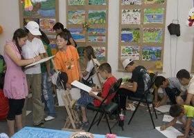 Children in a classroom engaging in an art activity, with some standing and others sitting and drawing.