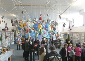 Indoor space decorated with large colorful hanging art installation, with children and adults walking around and observing.