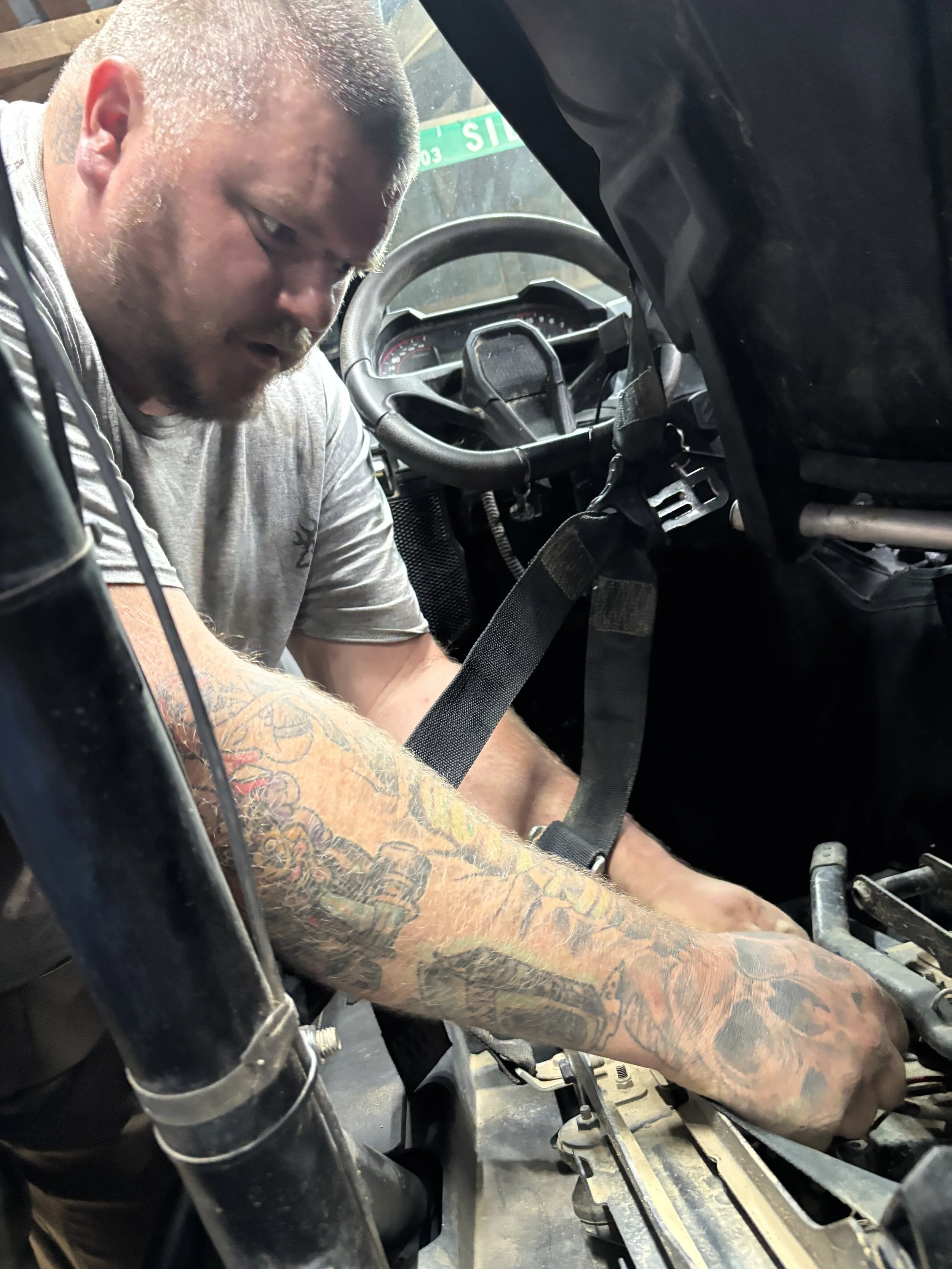 A man with tattoos working inside a vehicle, focusing on the dashboard area.