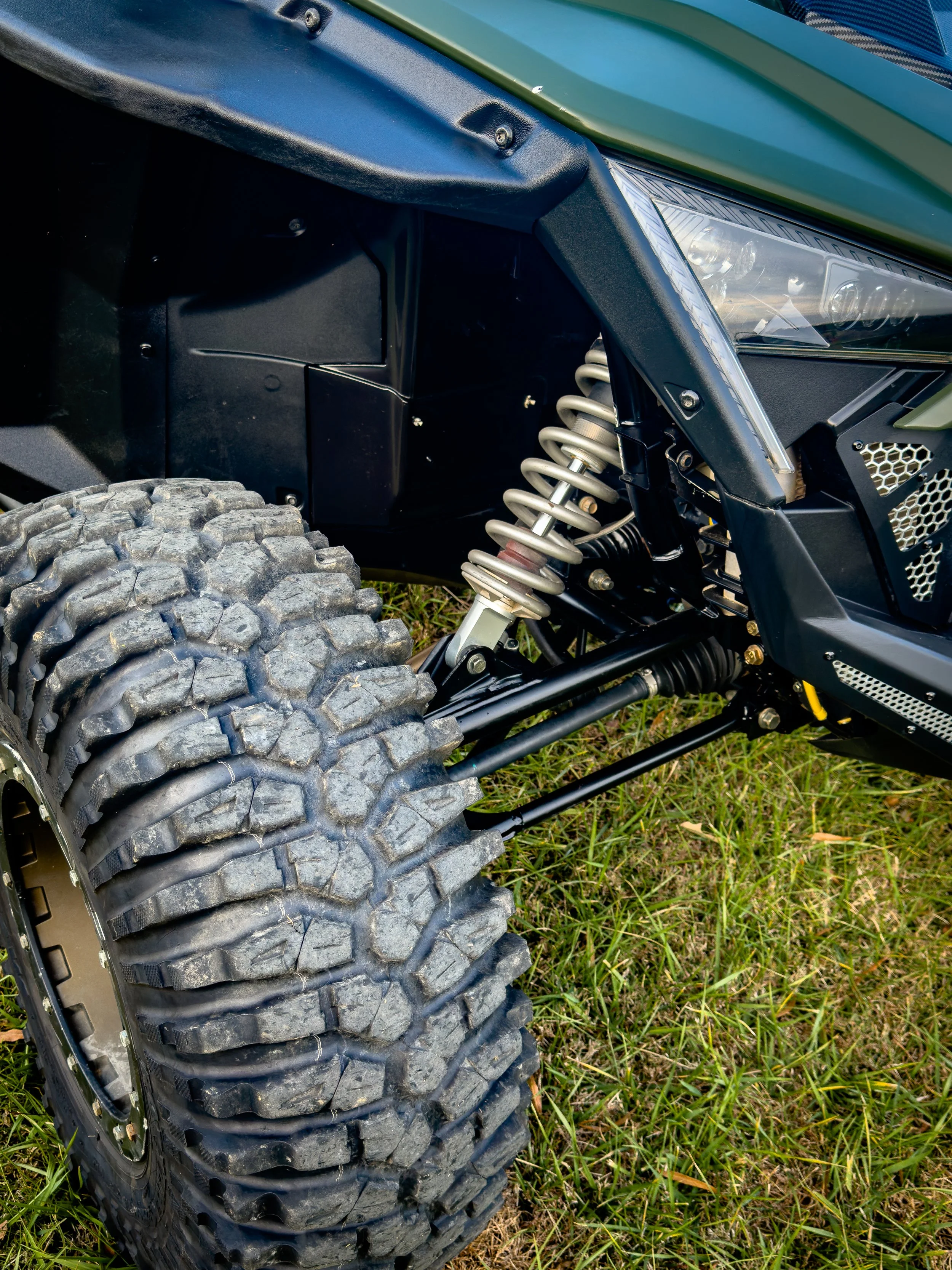 Close-up of off-road vehicle tire, suspension system, and front part, on grass.