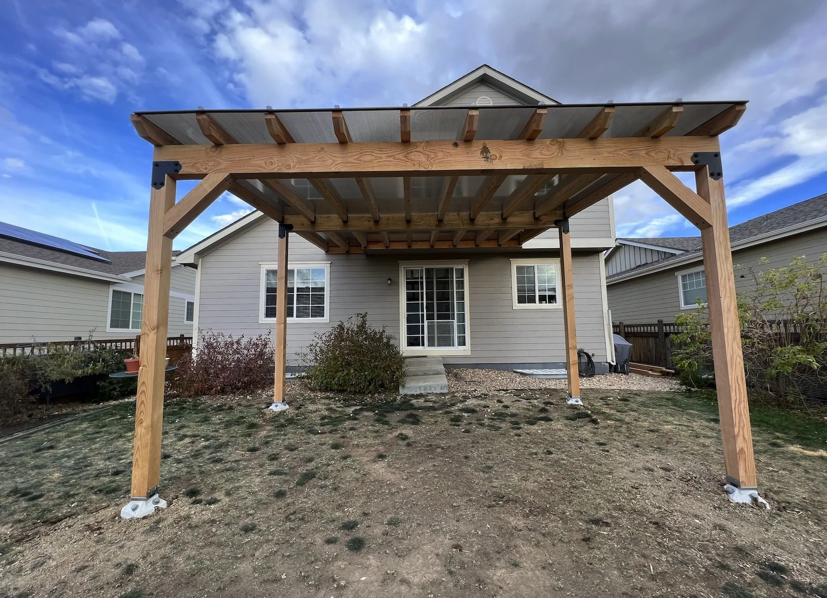 New wooden deck structure in backyard of a house under construction, with a cloudy sky in the background.