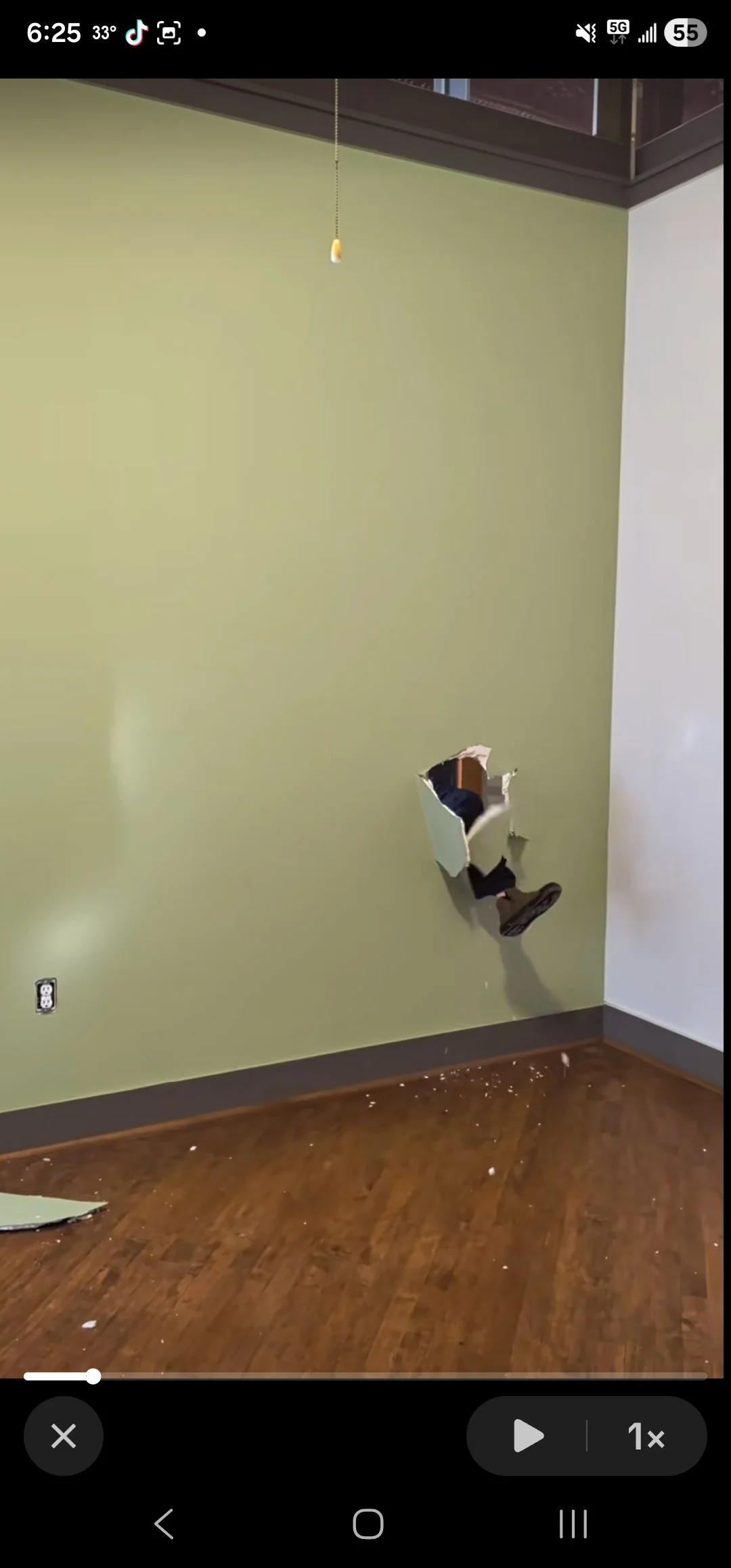 A person is falling through a large hole in a green wall, with debris on the wooden floor below.