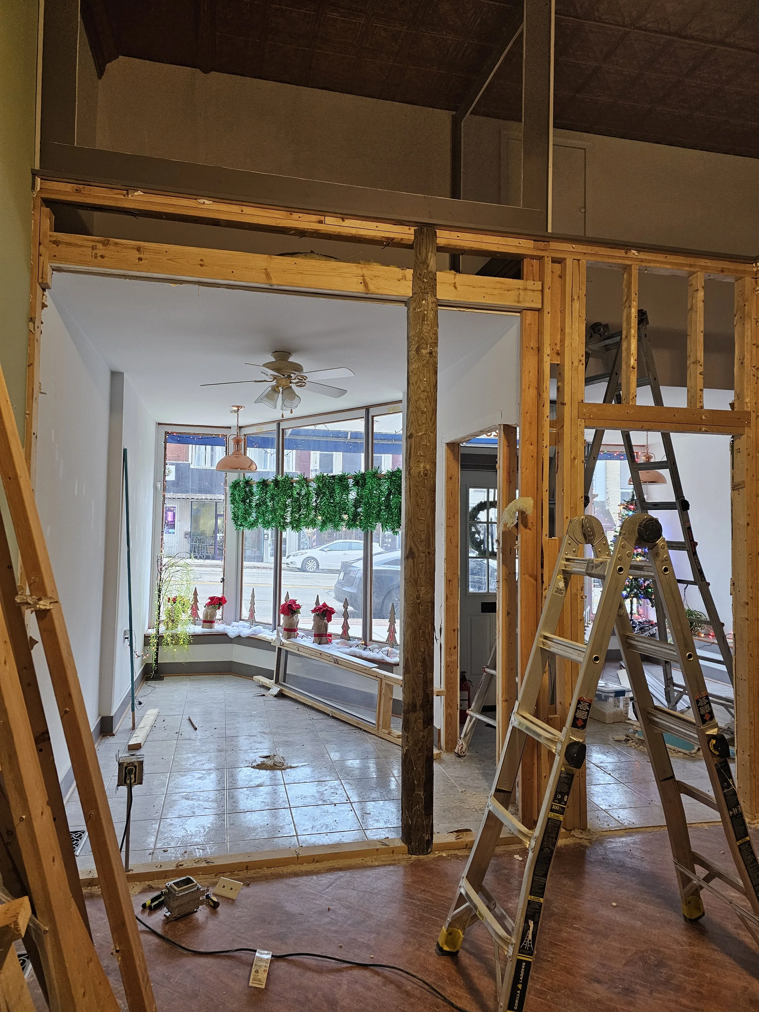 Interior under renovation with wooden framing, ladders, and a decorated window area with holiday decorations.