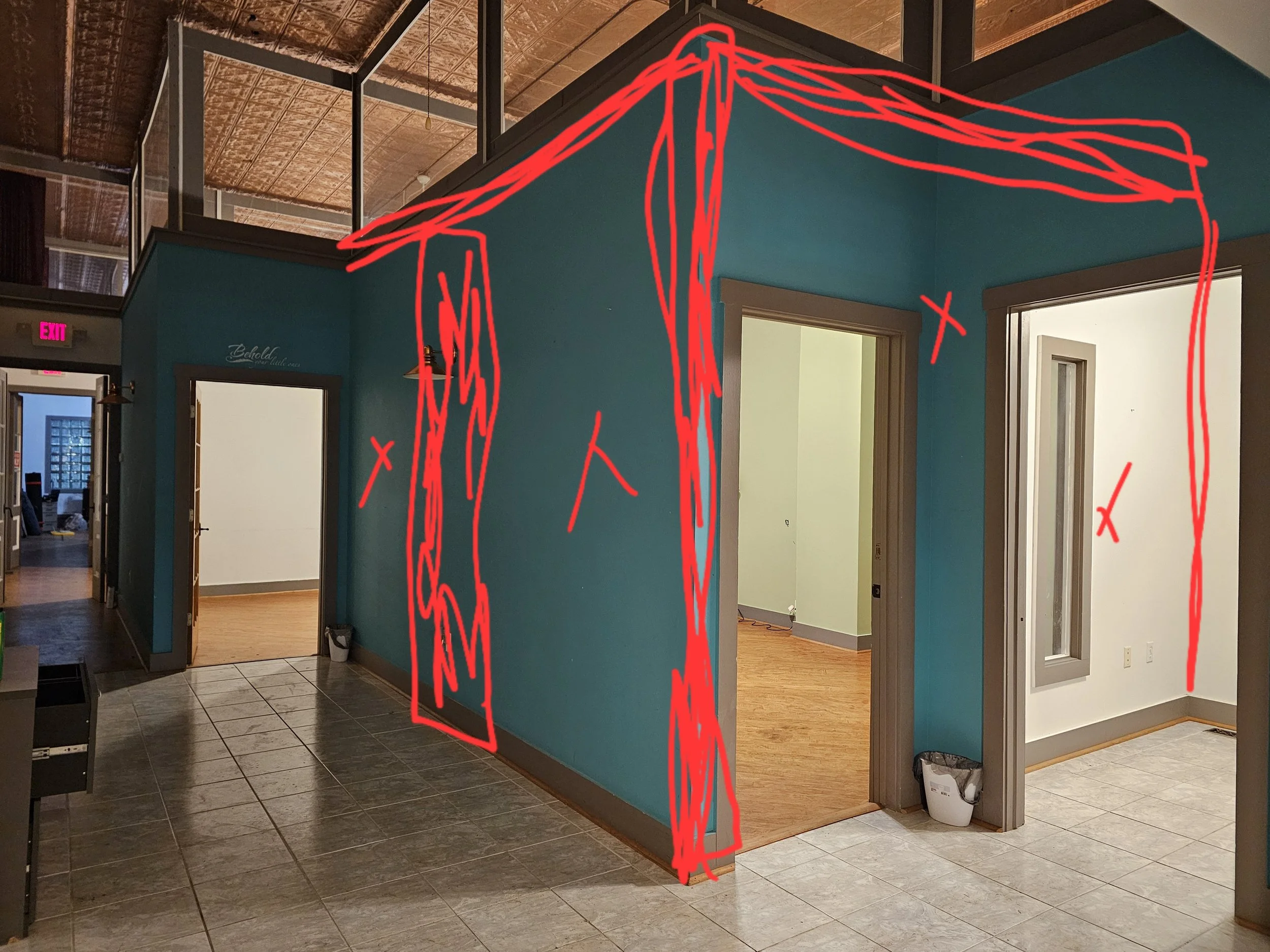 Interior of an office or commercial space with blue and white walls, tiled and wooden flooring, doorways, and a trash can, with red lines and X's drawn over part of the image.