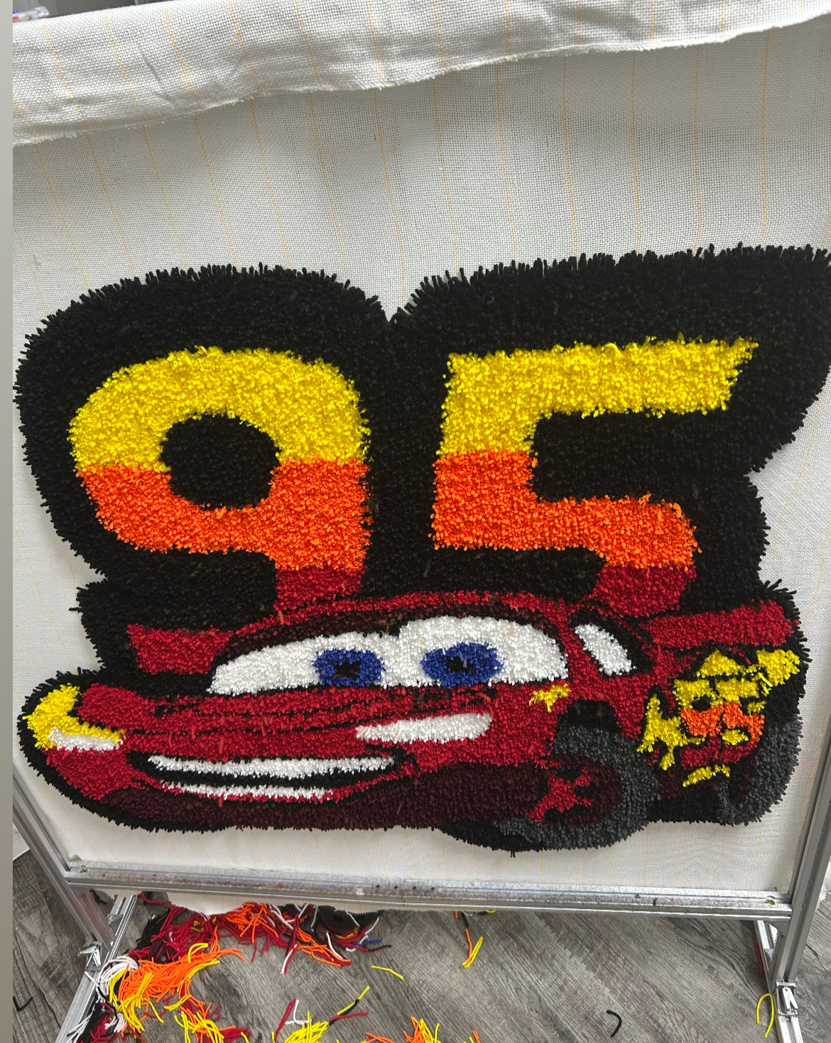 Colorful felt artwork featuring the number 95 and a cartoon race car with a smiling face and blue eyes.