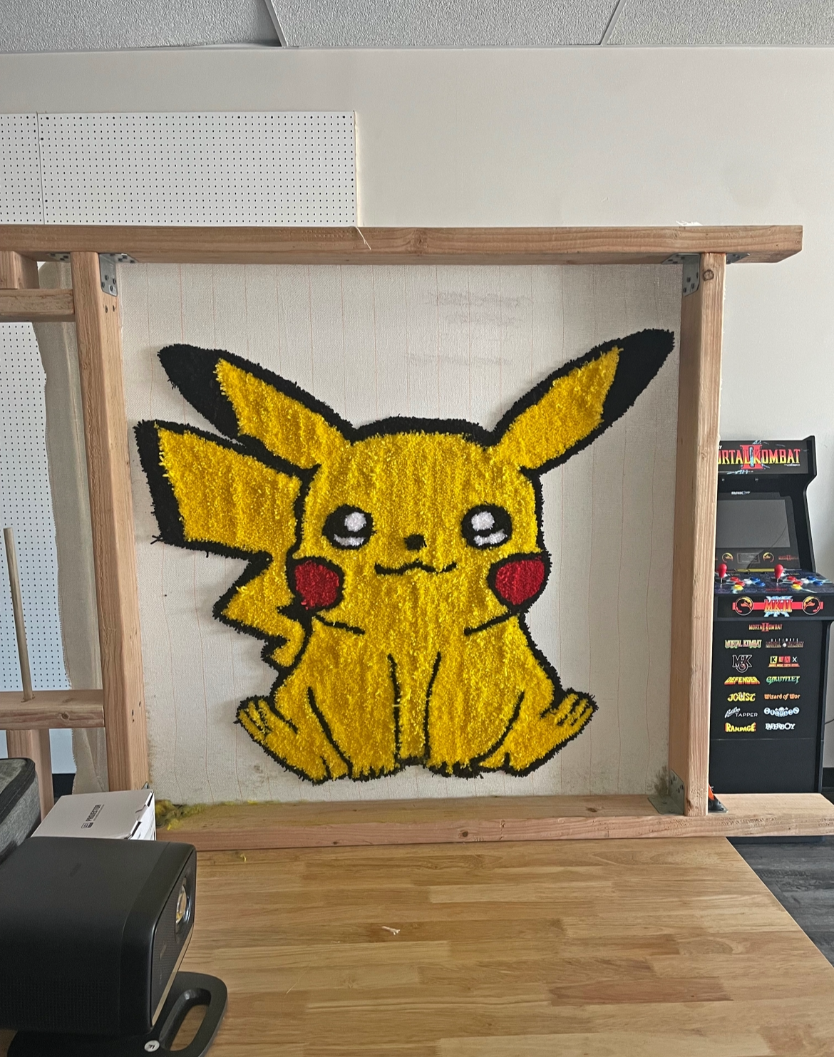 A Pikachu flower arrangement artwork made with yellow, black, red, and white flowers on a white background, framed by a wooden structure.