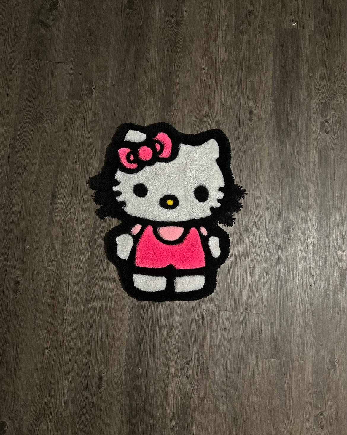 A hello kitty-themed rug on a wooden floor, featuring the character with a pink dress and bow.