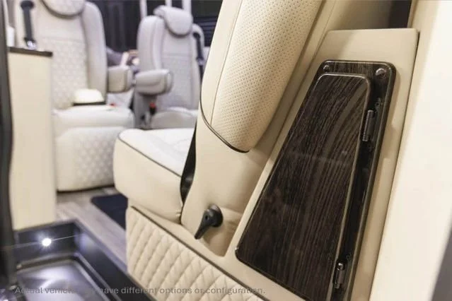 Close-up of an interior section of a luxury vehicle or airplane, showing a quilted beige upholstered seat with a small door or compartment and a dark wood panel.