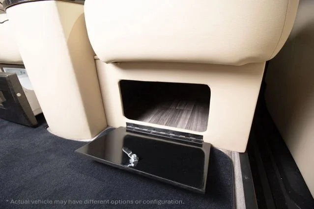 A black tray with a small plastic item on it, placed on a dark carpet near the back of a beige airplane seat with a storage compartment underneath.