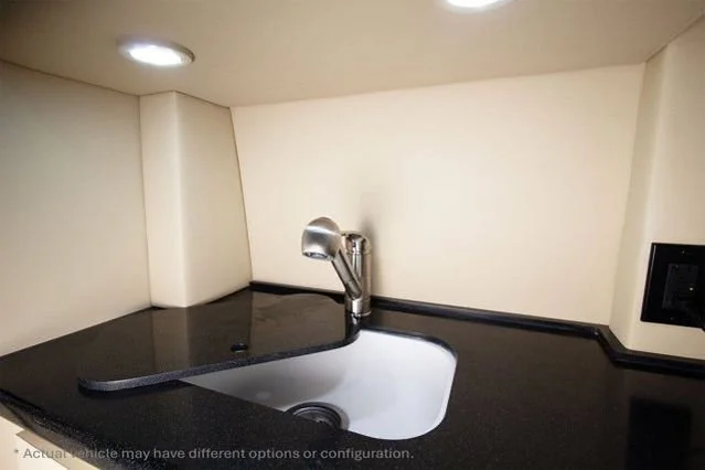 Small sink with a chrome faucet in a compact kitchen area with cream-colored walls and a black countertop.