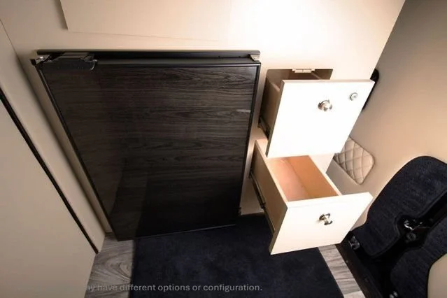 A foldable black table, a small beige cabinet with two drawers, one of which is open, and part of a black chair.