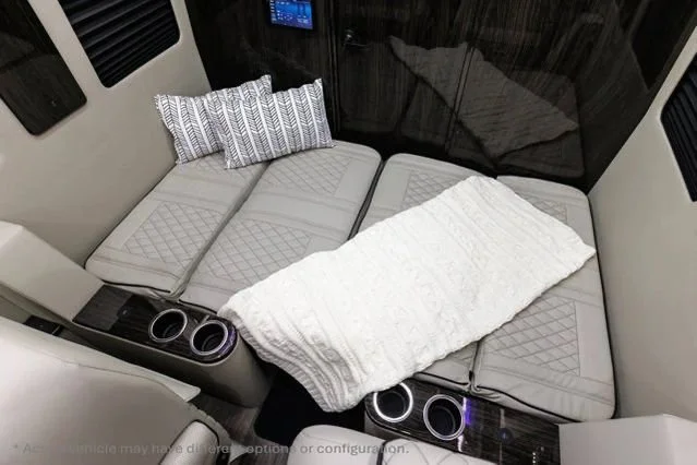 Interior of a vehicle with a flatbed made of seats, a blanket and pillows, suggesting a sleeping area.