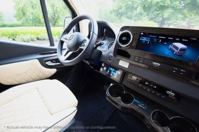 Inside the cab of a modern vehicle, showing a steering wheel, dashboard, digital display screen, and beige seat with quilted pattern.