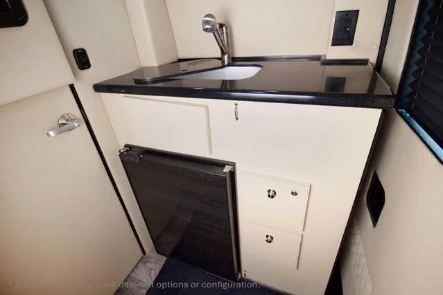 Small kitchenette with a black countertop, sink, and faucet, white cabinets, and a mini fridge, with a window and electrical outlets.