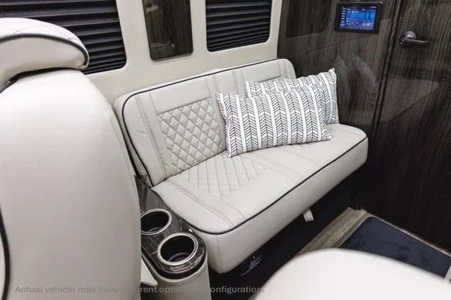 Interior of a vehicle with a white upholstered seat, quilted pillows, and built-in cup holders.