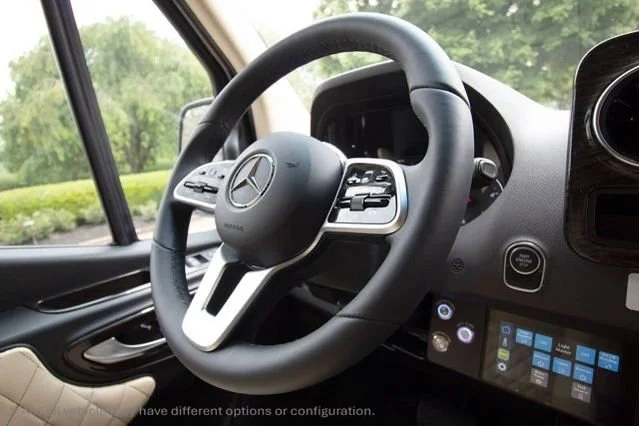 Close-up of the steering wheel and dashboard interior of a Mercedes-Benz vehicle with a digital display and control buttons.
