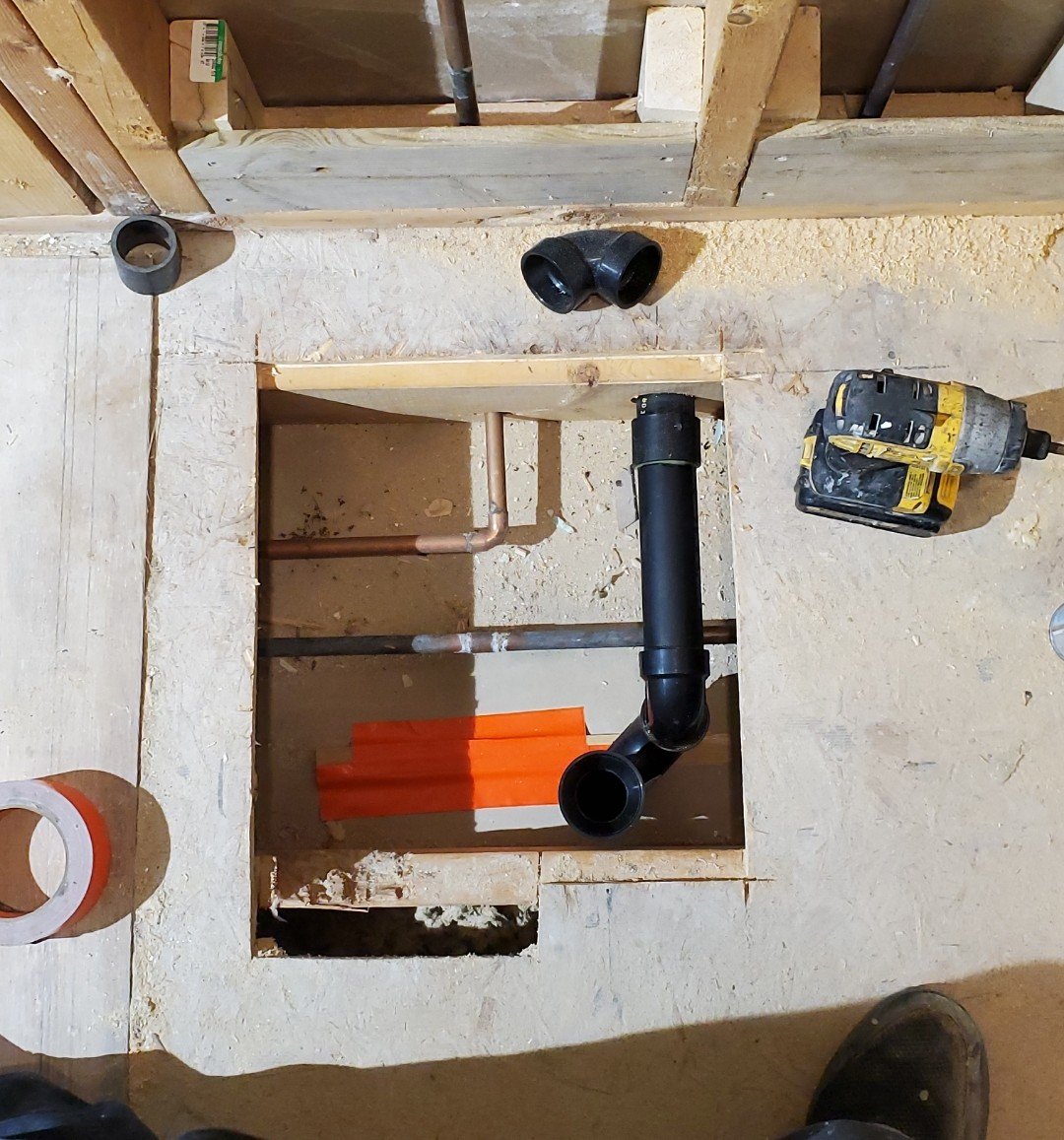 Installation of plumbing pipes in a construction site, with black plastic pipes, copper pipes, and a cordless drill on a wooden frame.