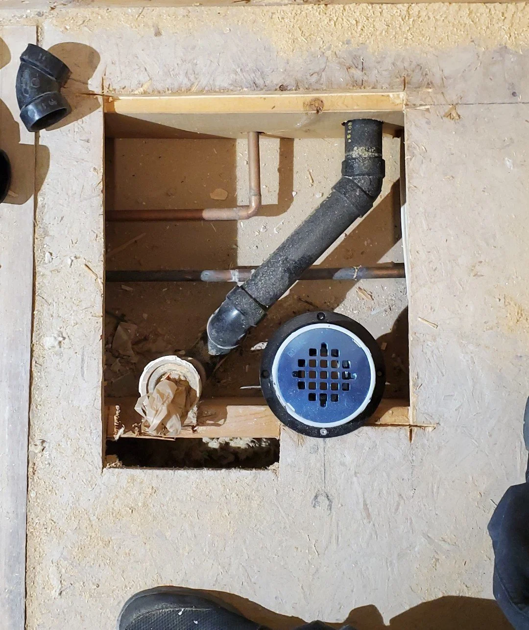 Open floor section exposing plumbing pipes and a drain with a metal cover.