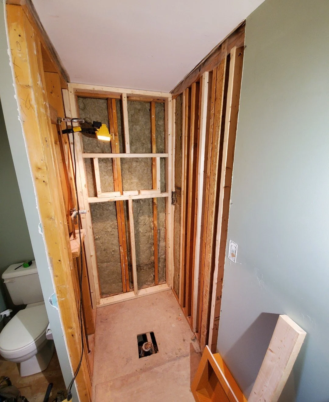 Bathroom in the process of renovation, showing framing of a wall with insulation and an exposed toilet on the left side.