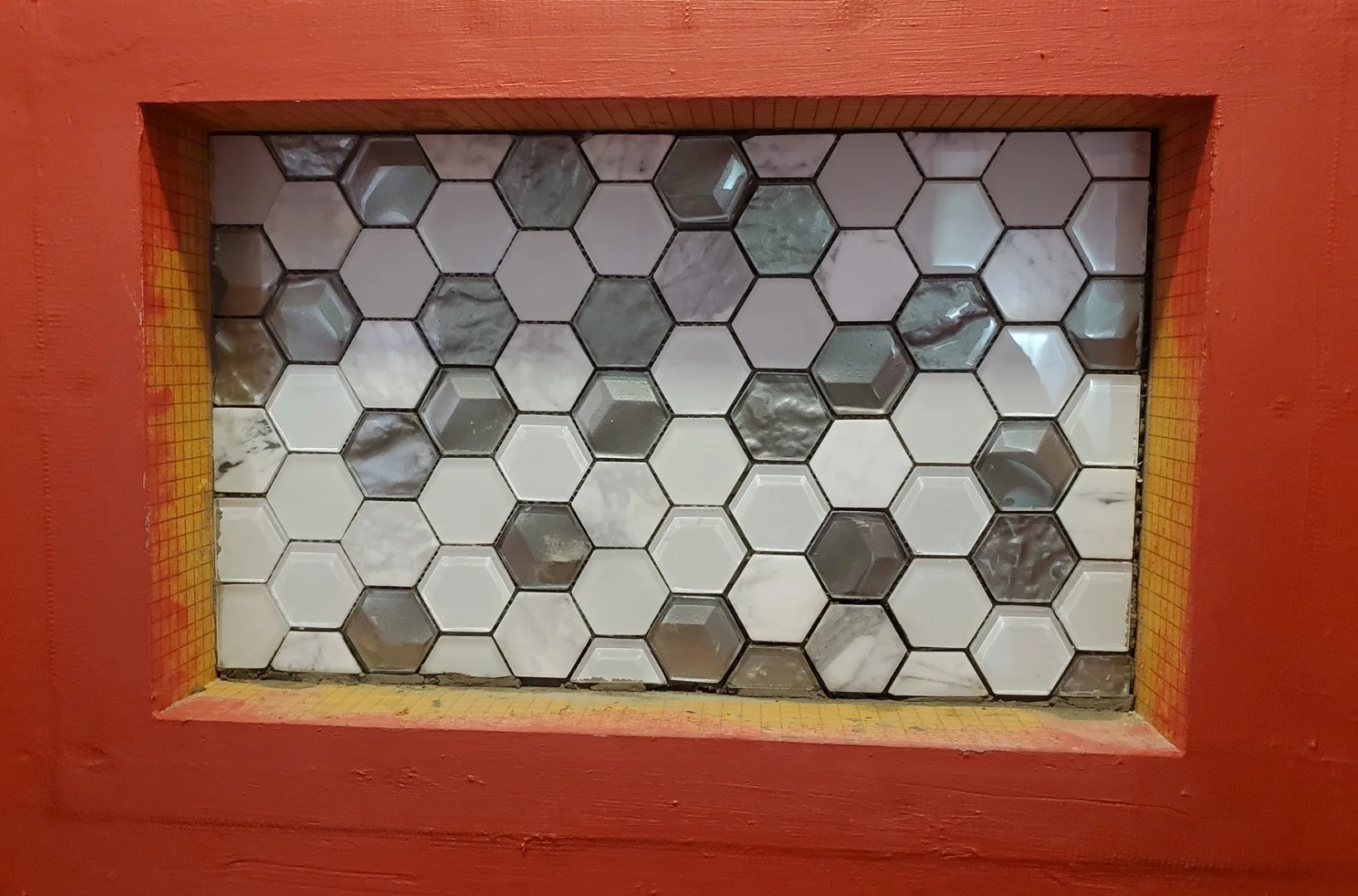 Decorative tile mosaic with black, white, and gray hexagonal tiles framed by a red border with yellow accents.