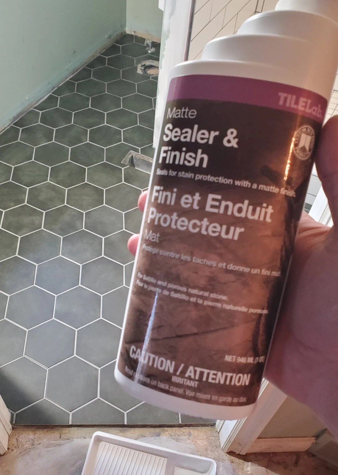 A can of matte sealer and finish for stain protection held by a person in a room with hexagonal tile flooring. The room appears to be under construction or renovation.