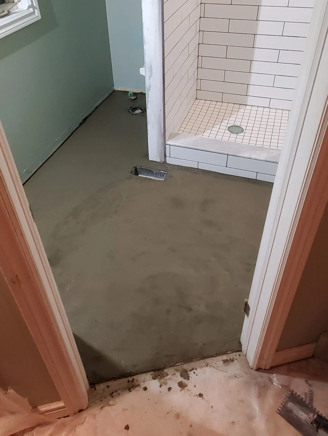Bathroom under renovation with a new shower stall and a concrete floor, with visible plumbing openings and construction tools.